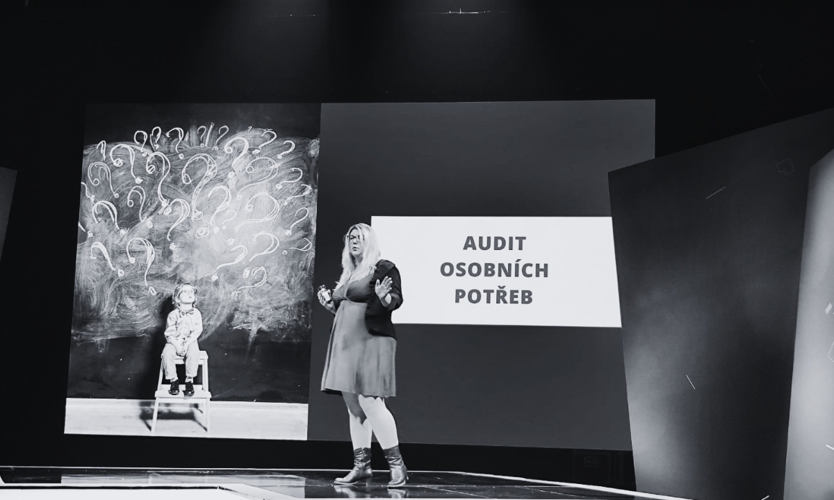 Dr. Alžběta Solarczyk Krausová speaking on stage beside presentation slides